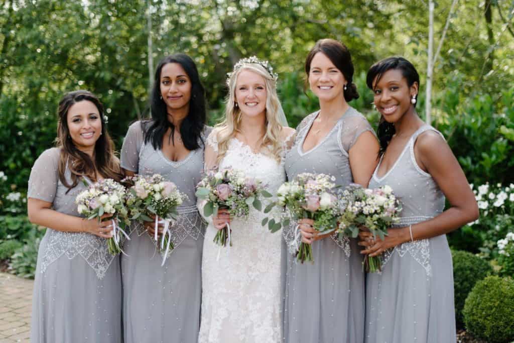 Bride poses with bridesmaids. They wear charcoal grey dresses