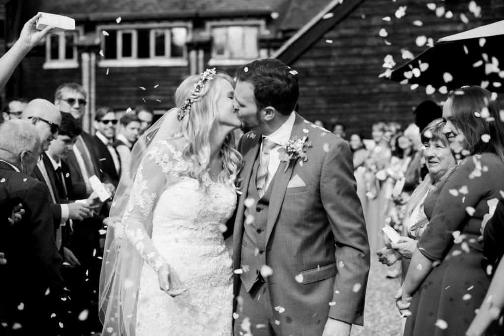 Black and white shot of bride and groom kissing among petal confetti